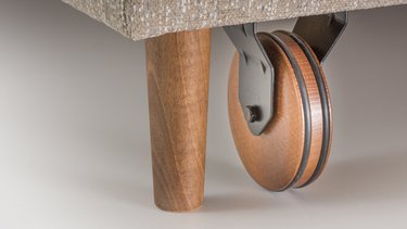 Nahaufnahme eines kegelförmigen Holzfußes mit einer daneben montierten Rolle aus Holz mit Gummiring.