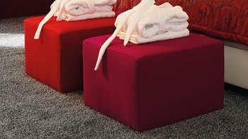 Weißes JOKA Noblesse Boxspringbett mit zwei roten Höckern und roter Wandgestaltung