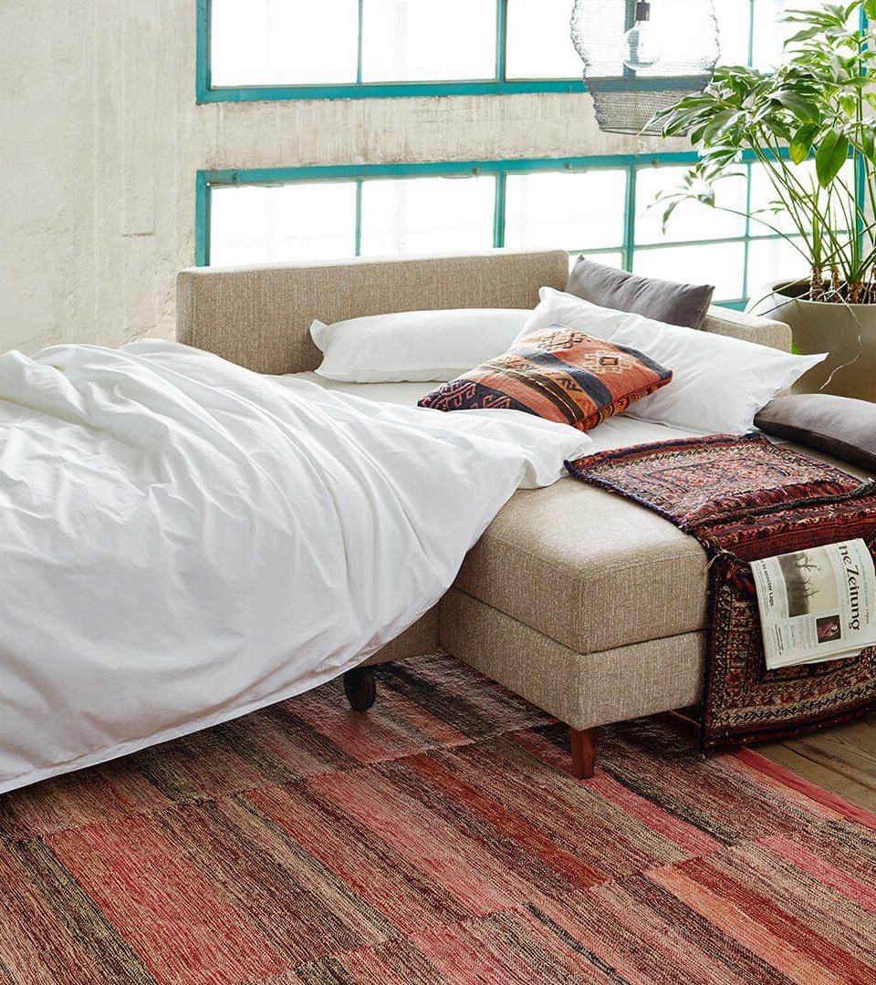 Zur Schlafstätte umgebautes Ecksofa mit weißem Bettzeug und Kissen in moderner Loft-Umgebung.