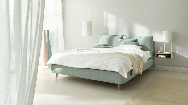 JOKA Arte Boxspringbett in Hellgrün mit weißer Bettwäsche und Holzfüßen im hellen Schlafzimmer
