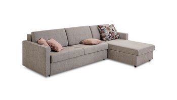 JOKA Marea L-förmiges Eckschlafsofa in Grau mit Récamiere, ausgestattet mit drei rosa Zierkissen und einem großen gemusterten Kissen, freigestellt auf weißem Hintergrund.