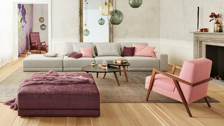 Joka Laguna großzügige graue Wohnlandschaft mit rosa Sessel, dunkelviolettem Hocker und Kamin