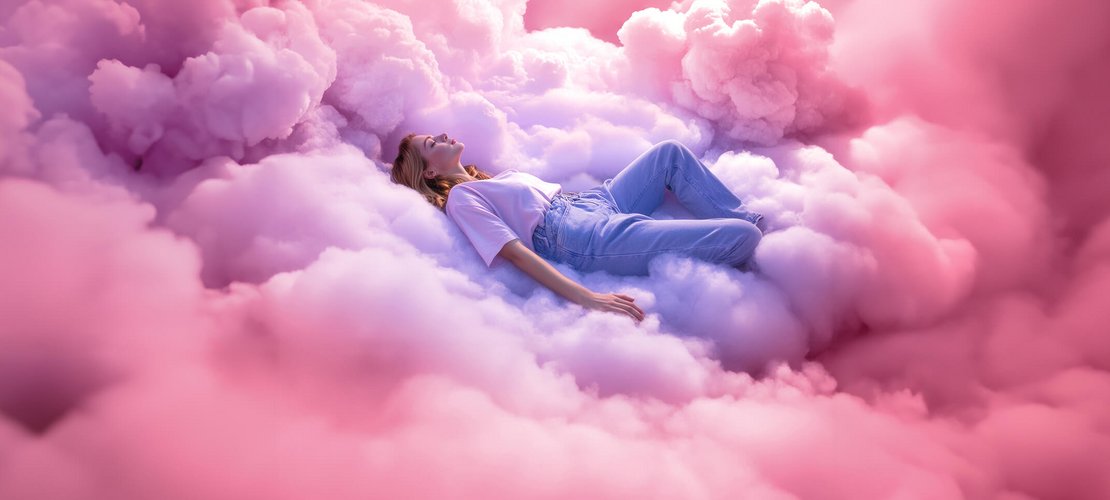 joka-airdream-flexinet-image.jpg      Eine Frau liegt entspannt in hellblauen Jeans und weißem T-Shirt auf rosafarbenen, bauschigen Wolken.
