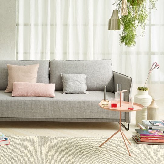 Hellgraue JOKA Lino Doppelliege mit passenden rosa und grauen Zierkissen in einem modernen Wohnbereich mit hellem Teppich und Beistelltisch.
