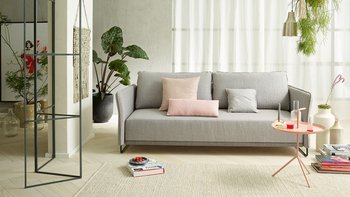 Hellgraue JOKA Lino Doppelliege mit passenden rosa und grauen Zierkissen in einem modernen Wohnbereich mit hellem Teppich und Beistelltisch.
