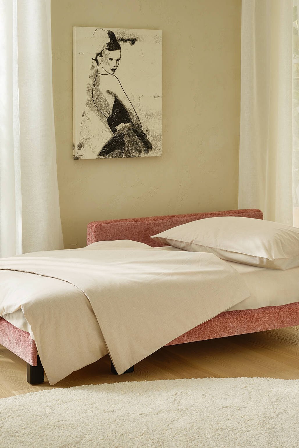Alternative Aufnahme der altrosafarbenen JOKA Recamiere in Bett-Konfiguration mit cremefarbener Bettwäsche im lichtdurchfluteten Hotelzimmer.