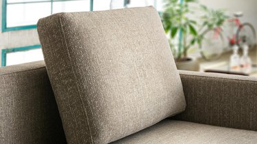 Detailansicht eines dick gepolsterten, kubischen Rückenkissens aus braun-beige meliertem Webstoff auf einem Sofa.
