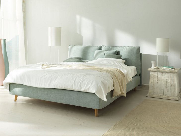 JOKA Arte Boxspringbett in Hellgrün mit Holzfüßen und hellem Holz-Nachttisch im lichtdurchfluteten Raum