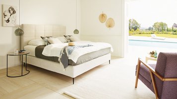 JOKA Mattina Boxspringbett in Hellbeige mit gepolstertem Kassetten-Kopfteil im sonnigen Schlafzimmer mit Poolblick