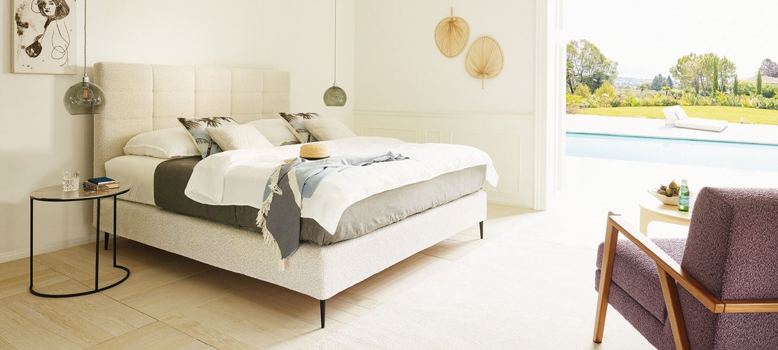 JOKA Mattina Boxspringbett in Hellbeige mit gepolstertem Kassetten-Kopfteil im sonnigen Schlafzimmer mit Poolblick