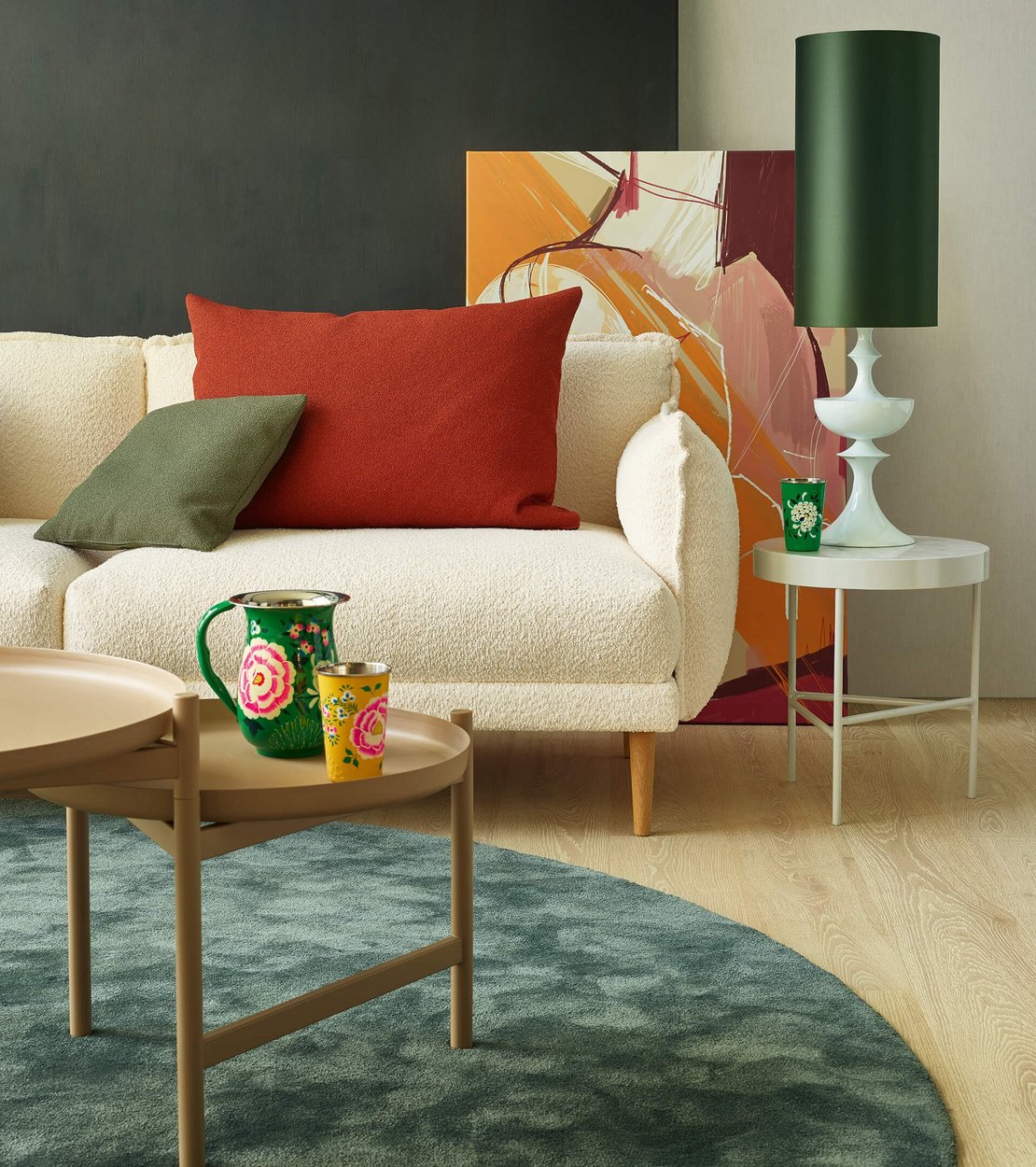 Hochformatiges Detailfoto eines weißen Bouclé-Sofas mit rotem und grünem Kissen neben einem Couchtisch.