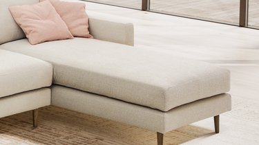 Detailansicht des Liege- bzw. Chaiselongue-Elements des hellem Sofas mit zwei rosa Kissen und Holzfüßen.