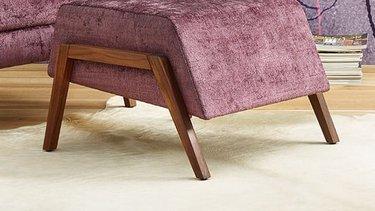 oka Laguna lilafarbener und rosa Fauteuil mit Hocker vor floral gemusterter Tapete