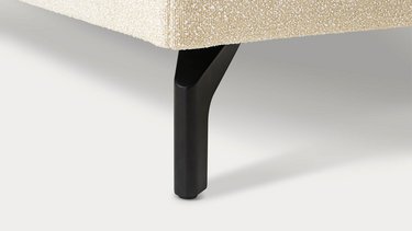 Detailaufnahme eines schräg angesetzten, schwarz-matten Metallfußes an der Unterseite des Sofas.