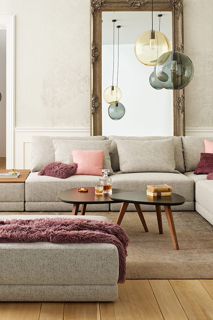 Joka Laguna helle Couchlandschaft in Grau mit dunklem Couchtisch und rosa Fauteuil im Hintergrund
