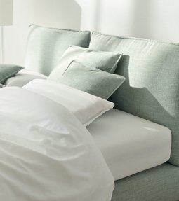 Helles Polsterbett mit lindgrünem Stoffbezug und weißen Kissen im modernen Schlafzimmer