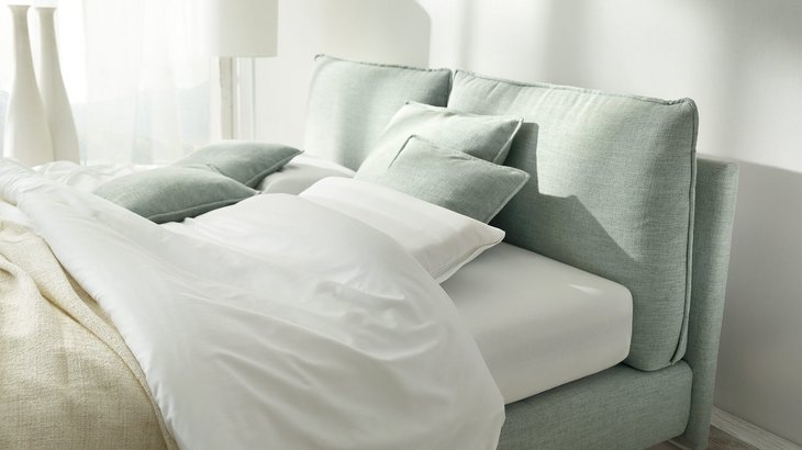 Helles Polsterbett mit lindgrünem Stoffbezug und weißen Kissen im modernen Schlafzimmer