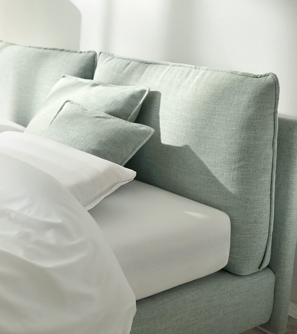 Helles Polsterbett mit lindgrünem Stoffbezug und weißen Kissen im modernen Schlafzimmer