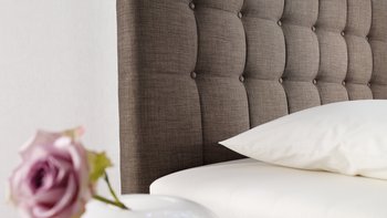 Detailansicht vom gepolsterten JOKA Noblesse Kopfhaupt in Braun mit eleganter Knopfheftung und weißem Kissen