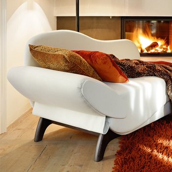 Geschwungenes Recamiere-Sofa in Weiß mit dunklen Holzbeinen und rustikaler Decke vor Kamin