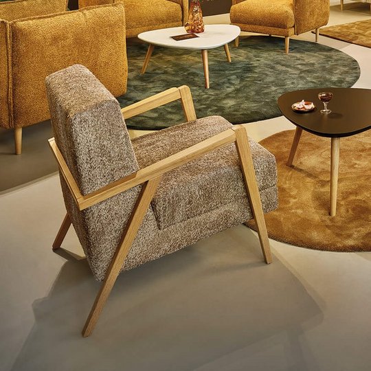 Gesamtansicht eines großzügigen JOKA Loungebereichs mit gelben und beigen Sesseln, Sofas sowie Holz-Beistelltischen auf verschiedenen Teppichen vor dunkler Wand und floraler Fototapete.