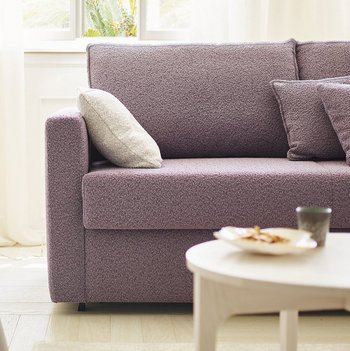 OKA Onda Doppelliege in Lila im Wohnzimmer mit passendem Sessel und Pflanzen.