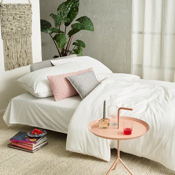 JOKA Lino Doppelliege umgebaut als gemütliches Bett mit weißer Bettwäsche, rosa und grauen Kissen in einem hellen Wohnraum.