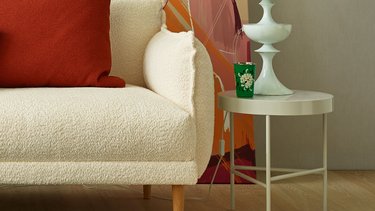 Nahaufnahme der soft gepolsterten Armlehne des weißen Bouclé-Sofas mit rotem Kissen und Beistelltisch.