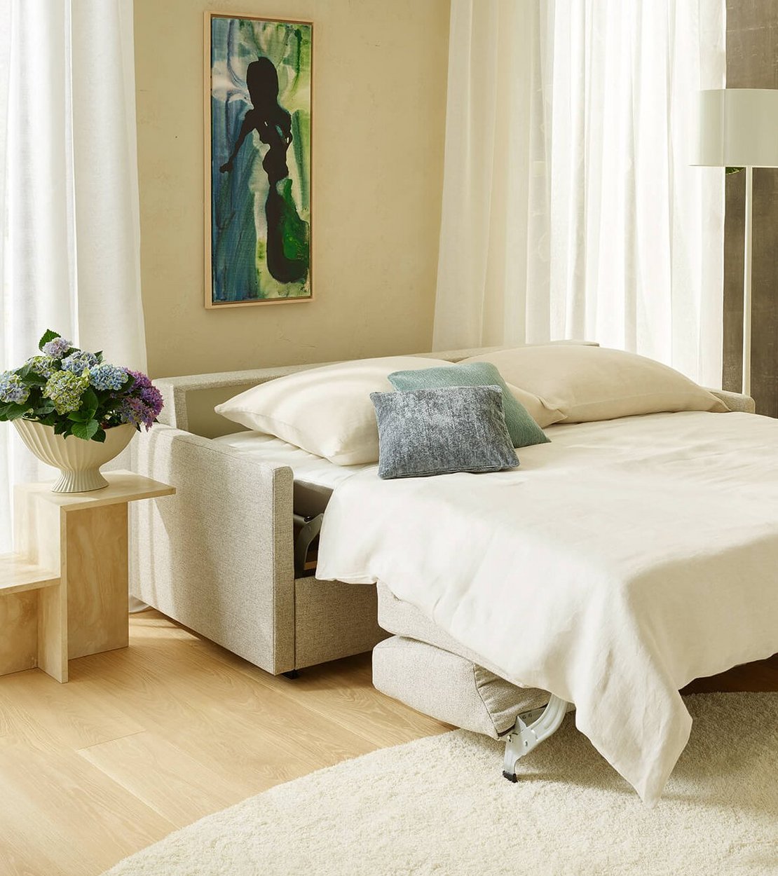 Ausgezogenes beigefarbenes JOKA Schlafsofa als Bett aufgestellt mit weißem Bettzeug und farblich abgestimmten Kissen im Hotelzimmer.