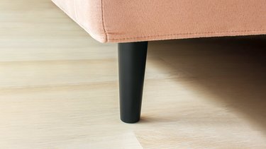 Nahaufnahme des schwarzen, leicht verjüngten Bettfußes am rosafarbenen JOKA Fiore Polsterbett im Hochformat.