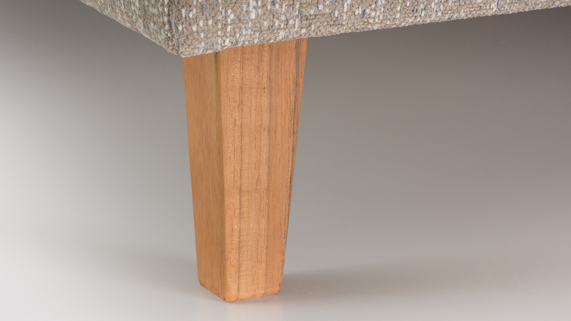 Detailaufnahme eines leicht verjüngten, quadratischen Holzfußes (Pyramidenfuß) in natürlicher Holzoptik unter dem Sofa.